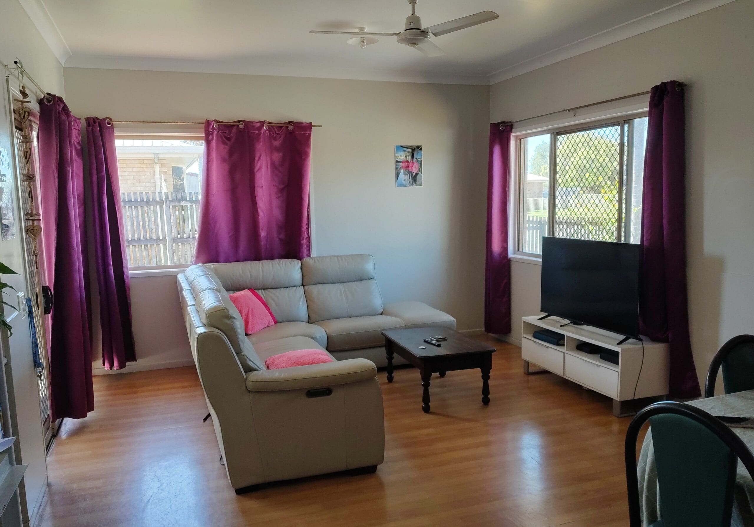 SIL Home in Mackay, Inverness Court Beaconsfield living room with sofa, TV, coffee table, timber-look flooring and purple curtains by Australia's leading disability accommodation provider.