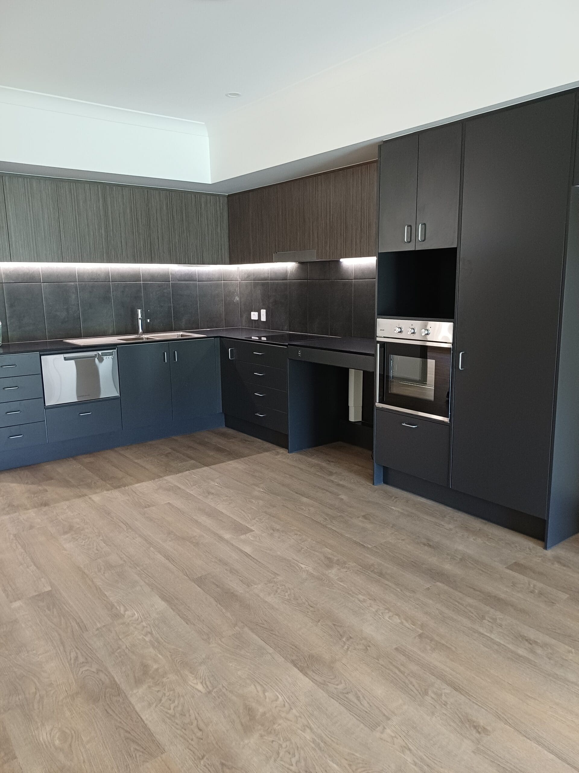 Accessible, modern kitchen in Purpose-Built High Physical Support Living in Cleveland, Langdon Street, featuring dark cabinetry, stainless steel appliances, and light wood flooring, part of Australia’s leading disability accommodation provider.