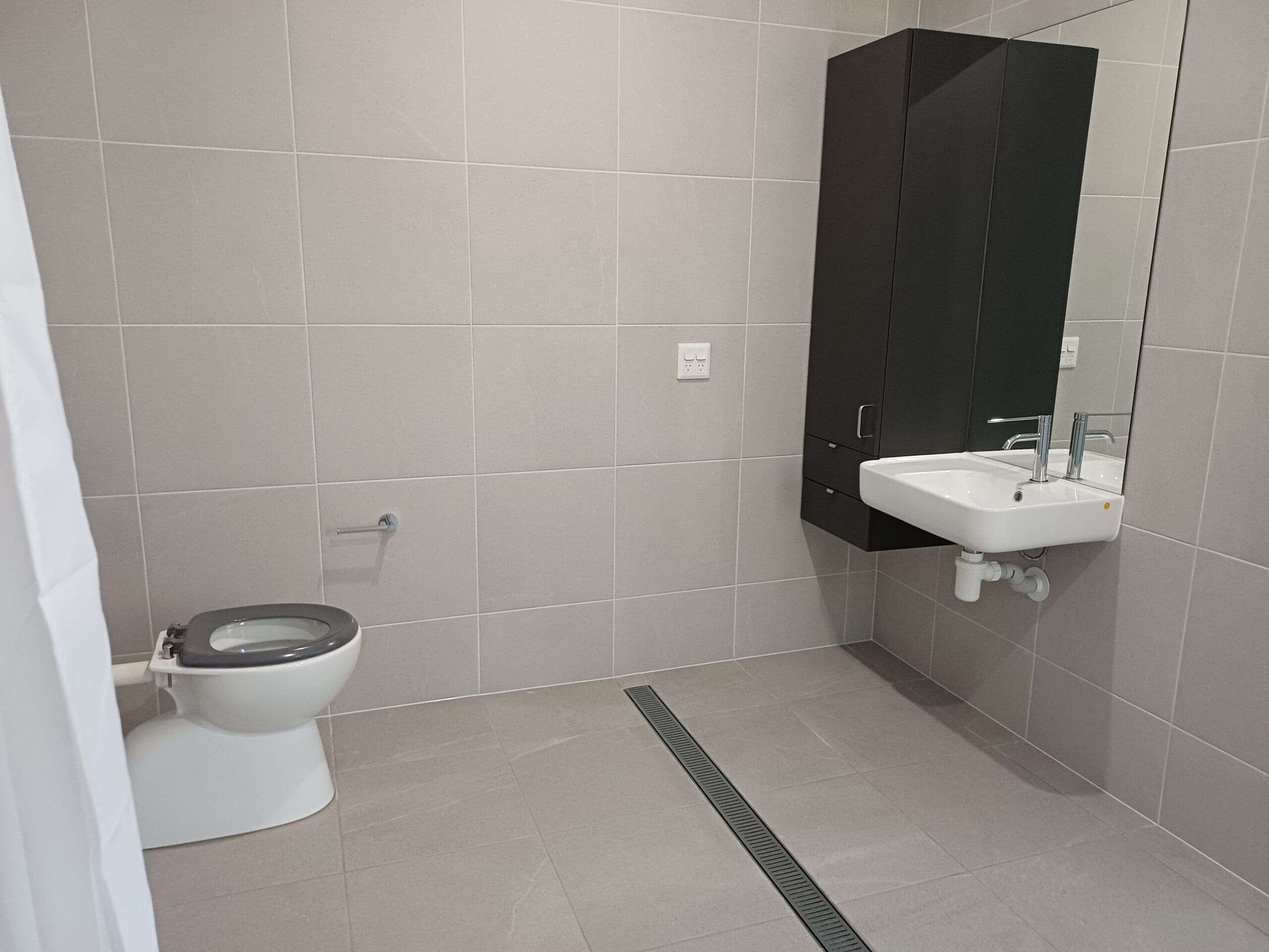 Accessible wet-area bathroom in Purpose-Built High Physical Support Living in Cleveland, Langdon Street, featuring walk-in shower, wall-mounted sink, and grab rails, part of Australia’s leading disability accommodation provider.