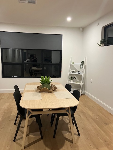 Dining area in brand-new SDA home in the heart of Morphett Vale, Kenwood Dr, featuring light wood table, black chairs, and ladder shelf, part of Australia’s leading disability accommodation provider.