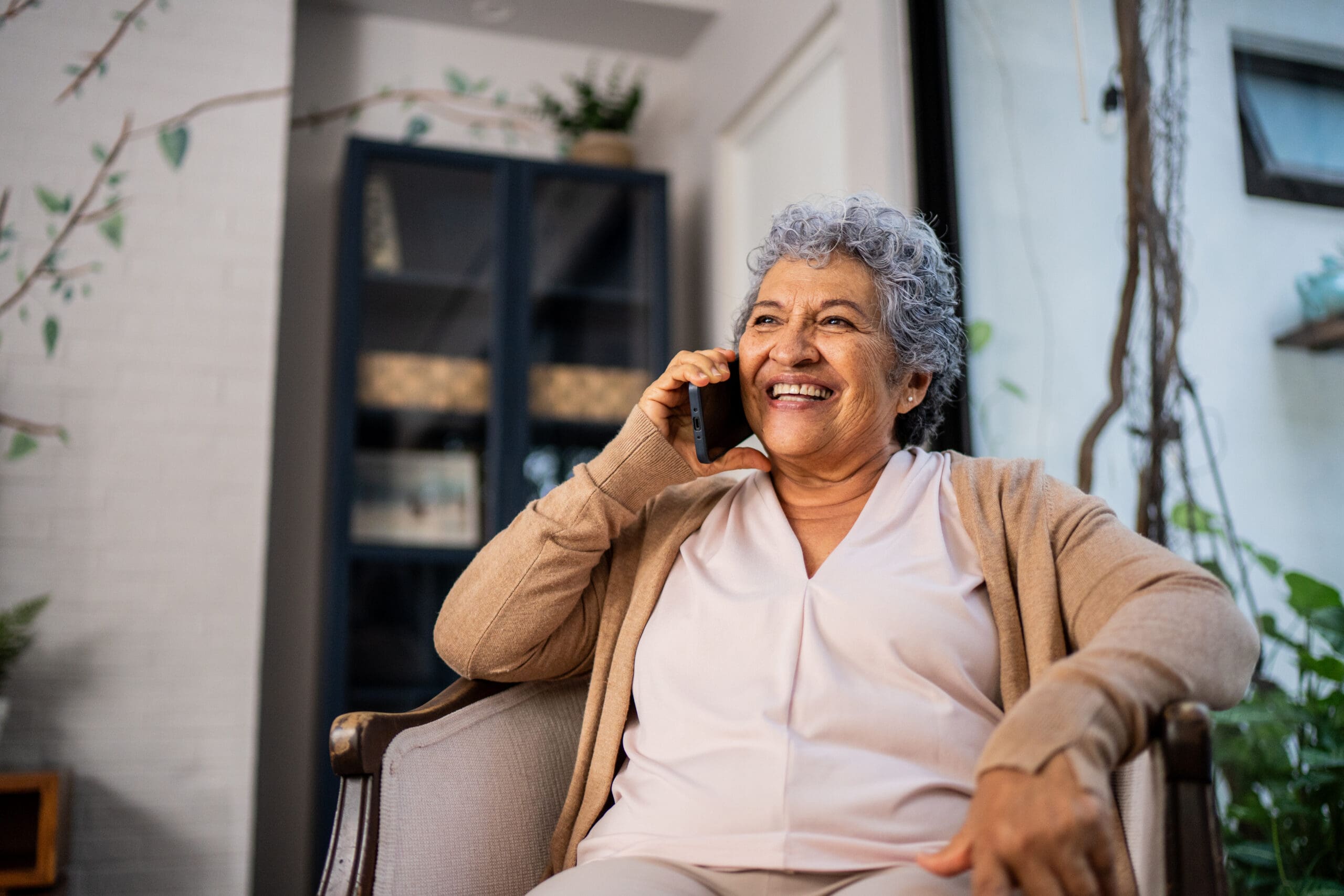 Senior woman talking on call at home while sitting comfortably in an armchair and smiling.