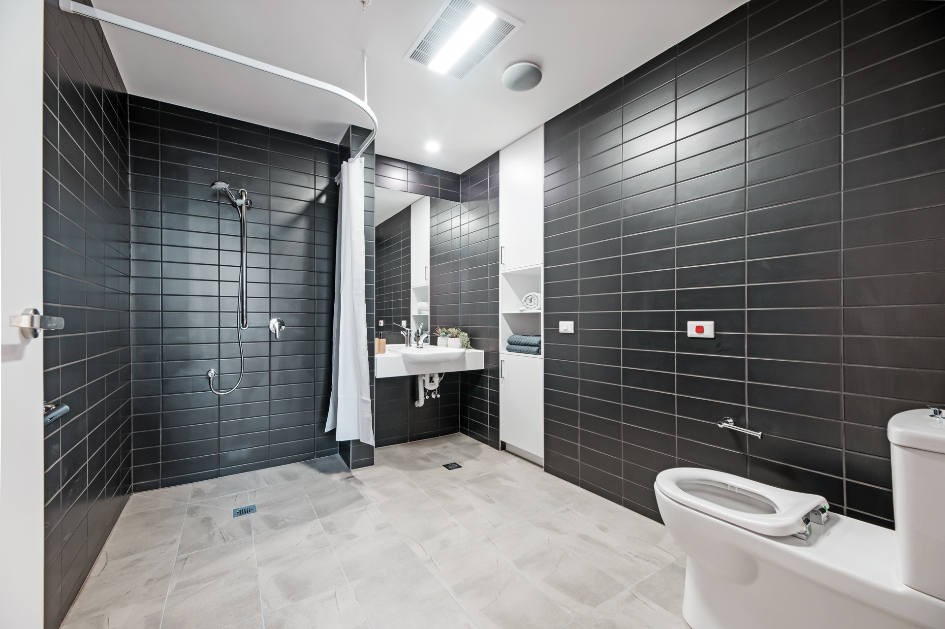 La Scala Avenue accessible bathroom with open shower, ceiling hoist track, wall-mounted basin and toilet by Australia's leading disability accommodation provider.