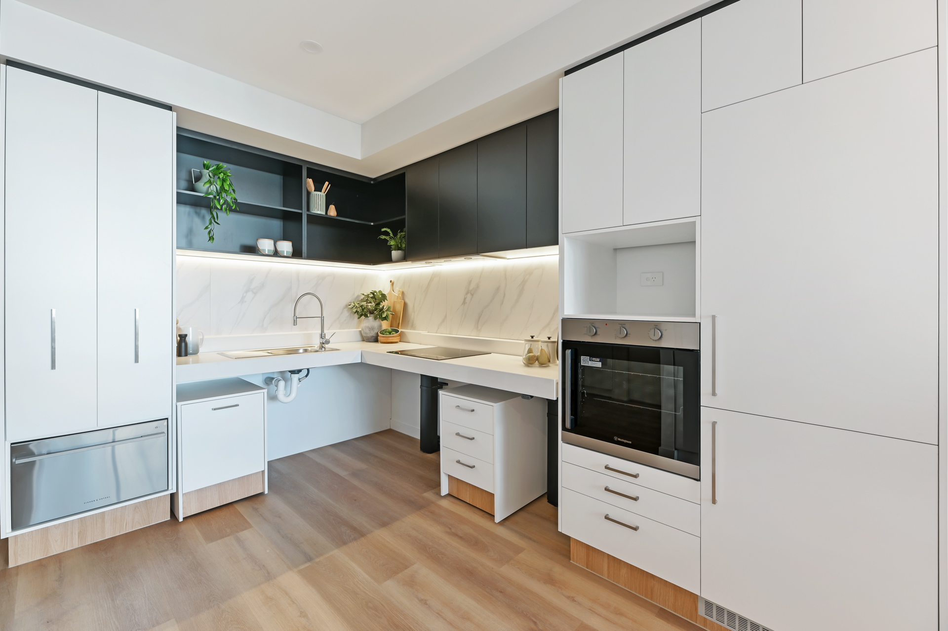 La Scala Avenue accessible kitchen with open sink space, white cabinetry, built-in oven and timber-look flooring by Australia's leading disability accommodation provider.
