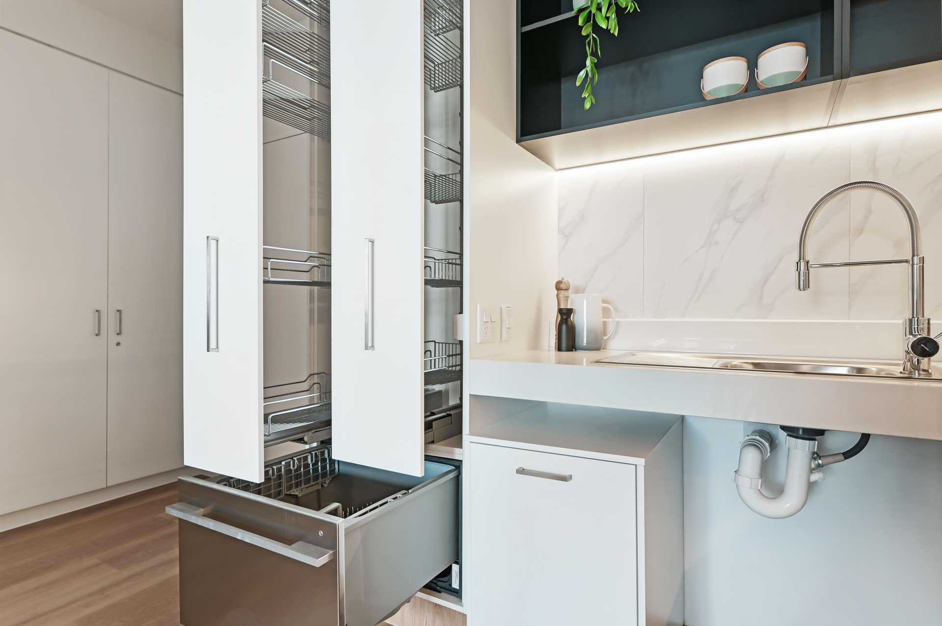 La Scala Avenue accessible kitchen with pull-out pantry, open sink space, white cabinetry and timber-look flooring by Australia's leading disability accommodation provider.