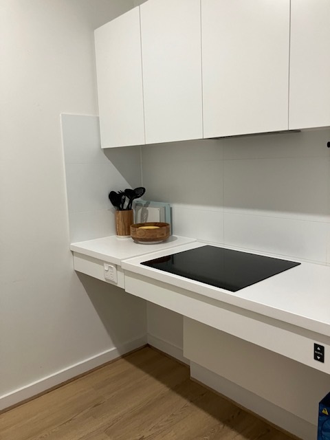 SDA Villa in Fullarton kitchenette with white cabinetry, cooktop, utensil holder and wooden bowl by Australia's leading disability accommodation provider.