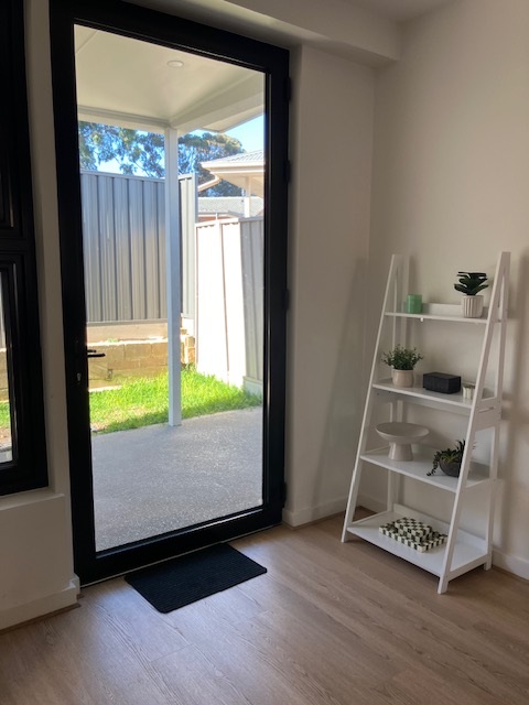 SDA Villa Patio access in Fullarton room with glass door to courtyard, timber-look flooring and white display shelf by Australia's leading disability accommodation provider.