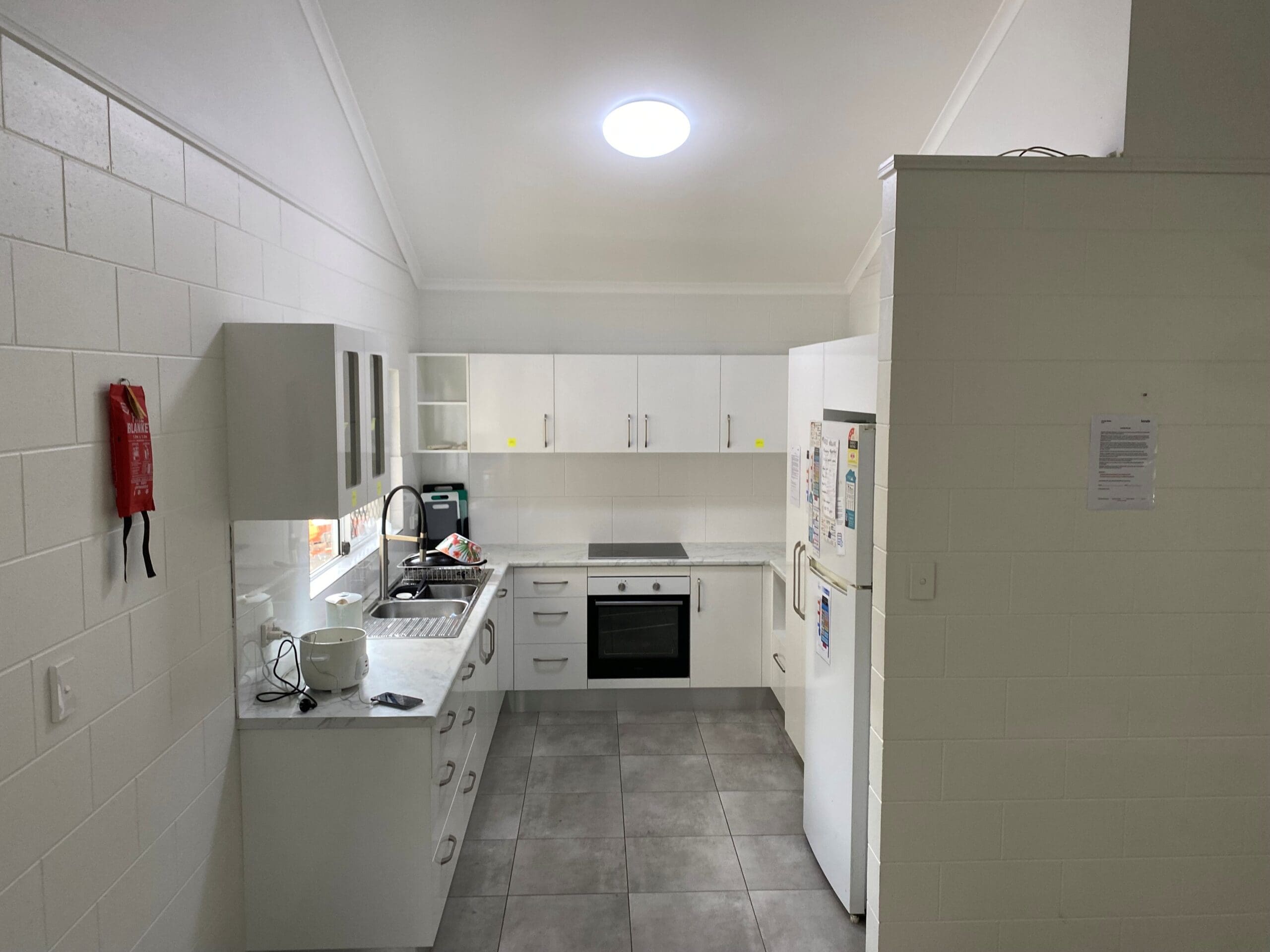 SIL Vacancy in Bentley Park, Cairns, Lorraine Close, Bentley Park kitchen with white cabinetry, sink, fridge, oven and grey tiled floor by Australia's leading disability accommodation provider.