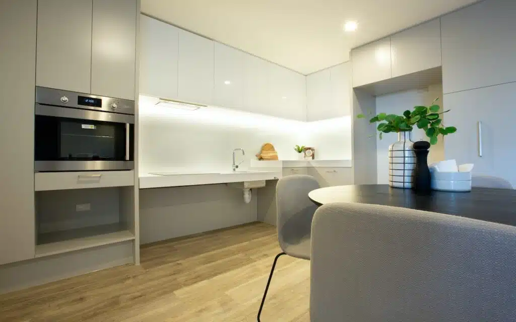 New SDA apartments in the heart of Joondalup with OSS, Grand Blvd, Joondalup kitchen and dining area with accessible sink, built-in oven and round table by Australia's leading disability accommodation provider.