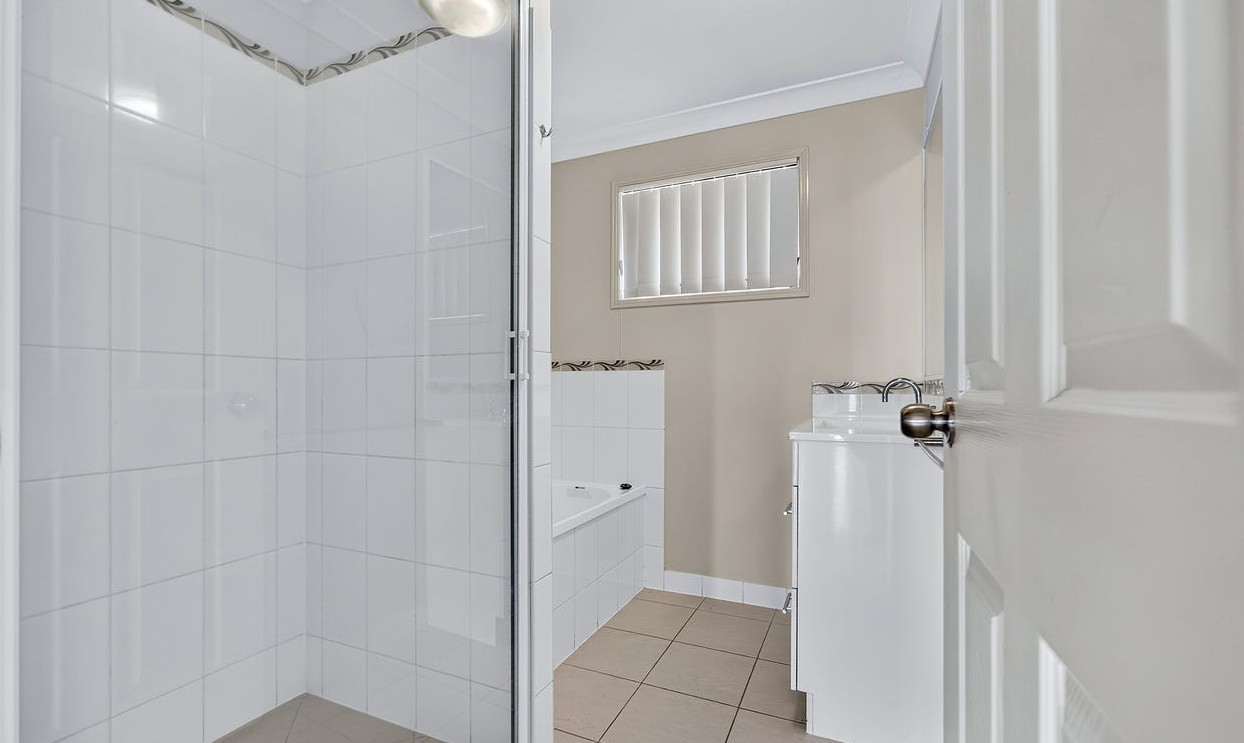 Roomy SIL home in Gracemere, Joseph St Gracemere bathroom with glass shower, bathtub, vanity and window blinds by Australia's leading disability accommodation provider.