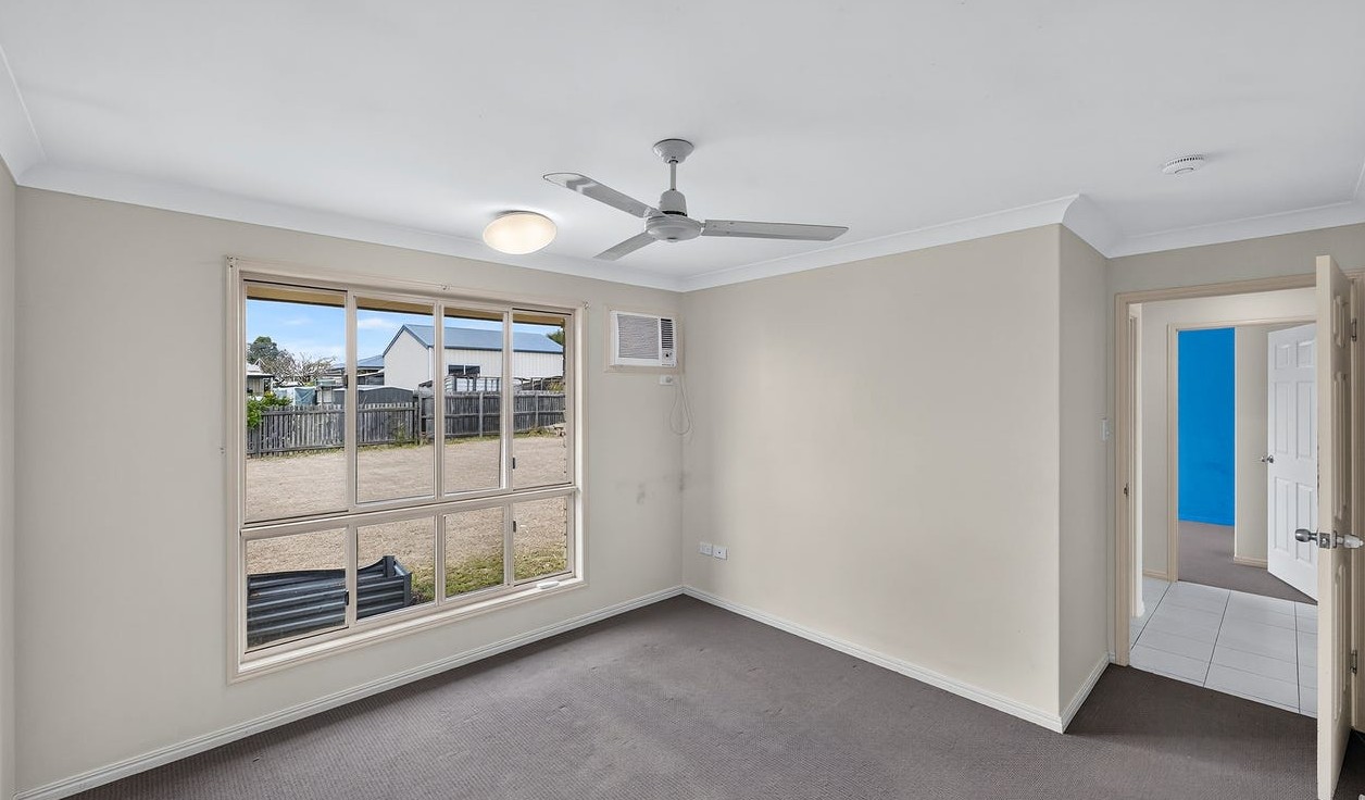 Roomy SIL home in Gracemere, Joseph St Gracemere bedroom with carpet, ceiling fan, window, air conditioning and hallway access by Australia's leading disability accommodation provider.