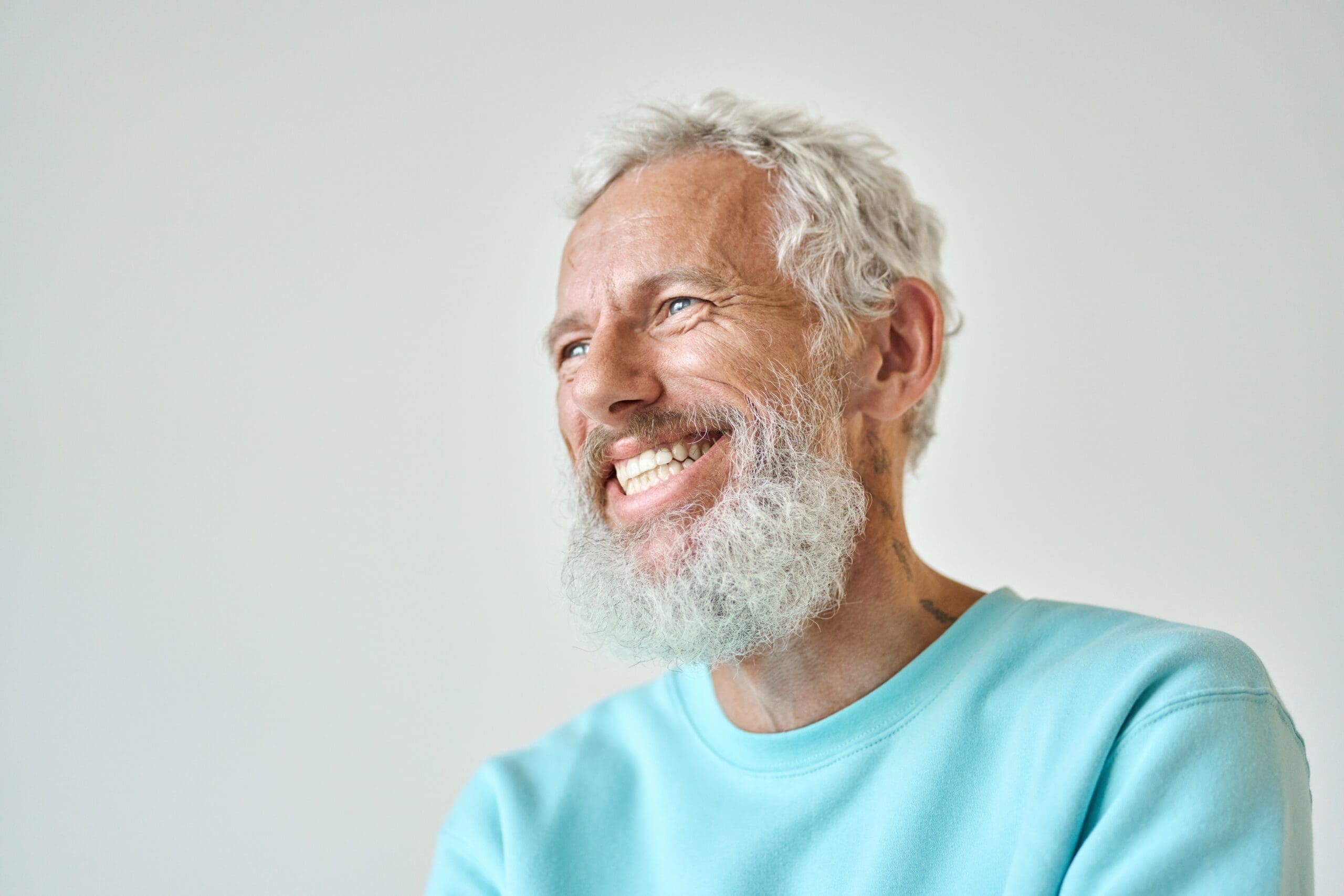 Older man with grey hair and a full beard laughing and wearing a light blue shirt